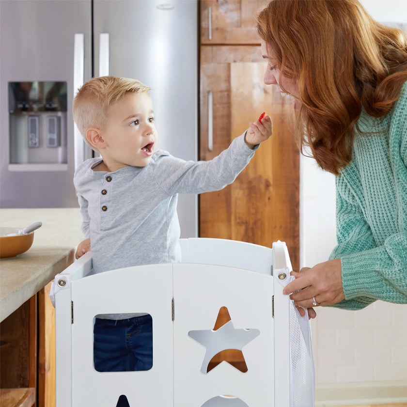A young boy offers food to a smiling woman while standing in a white kitchen helper stool.
