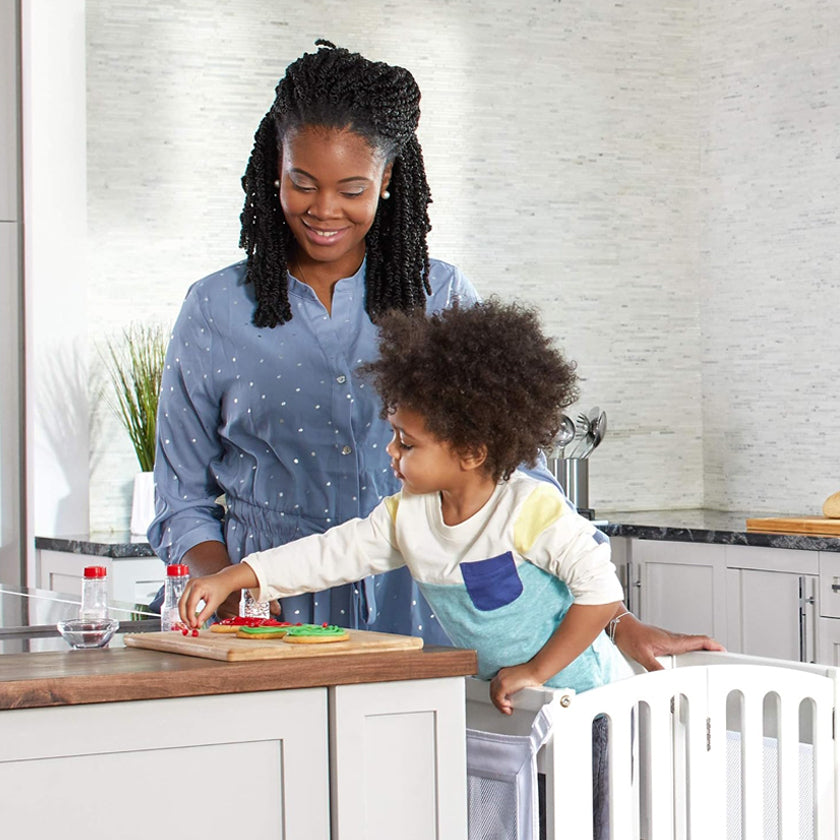 A woman and child smile together in a kitchen while preparing food on a wooden cutting board.