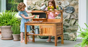 Two preschool-aged girls using a child-sized potting bench made of acacia wood
