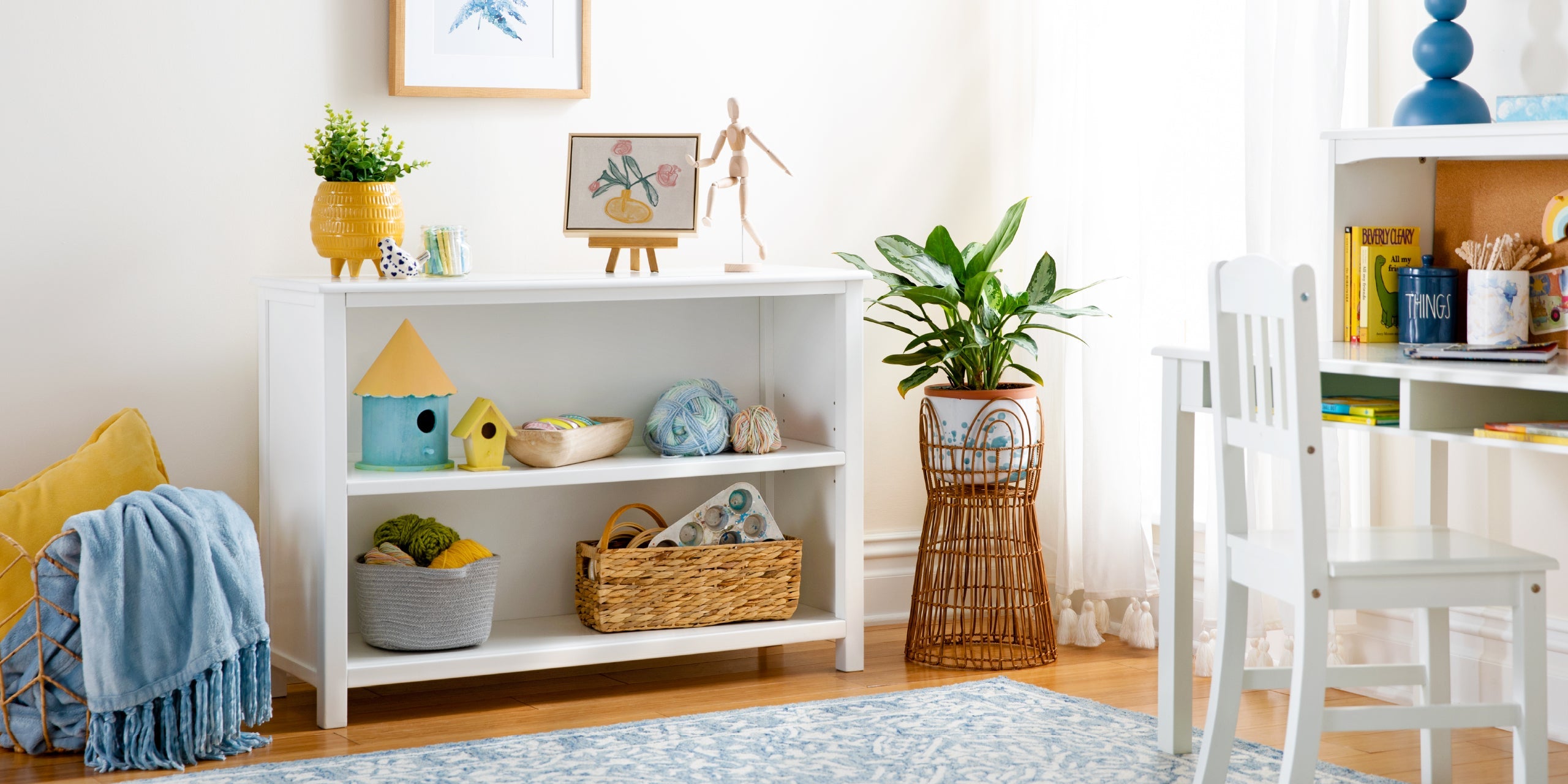 Bright, cozy playroom with a white shelf, plants, toys, books, and a chair on a blue patterned rug.