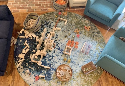 A round rug with scattered building blocks and toys, surrounded by cozy blue chairs and a comfortable sofa.