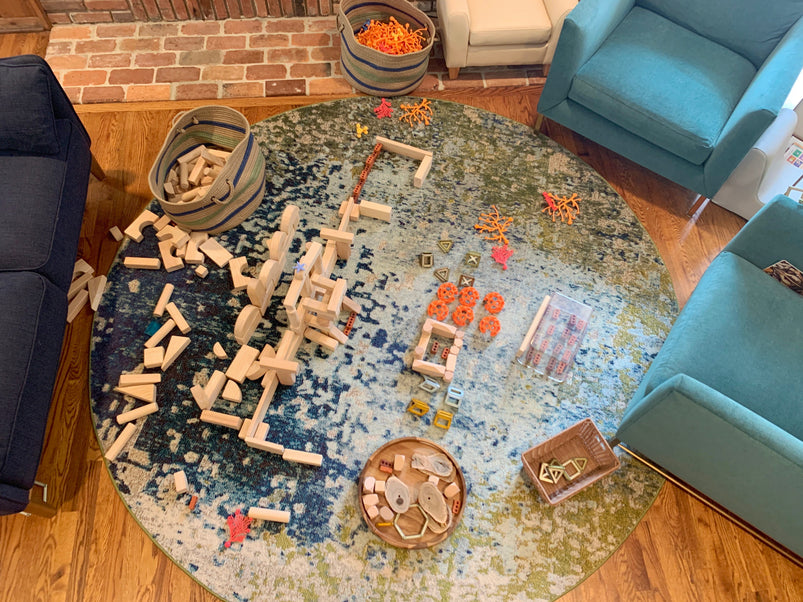 Colorful childrens building blocks and toys are scattered on a round rug in a cozy living room with blue chairs, creating a playful and inviting space.