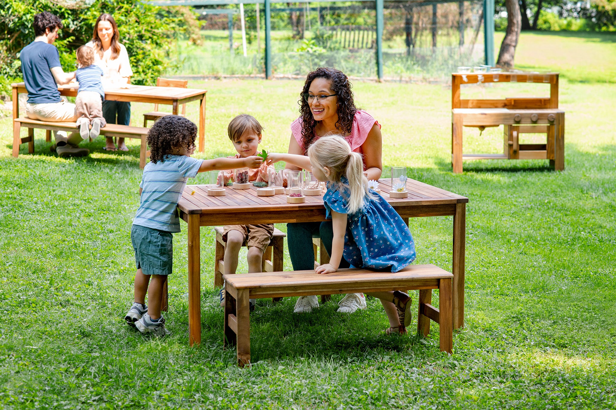 Children playing with a wooden outdoor table in a park setting. Click to shop all outdoor furniture.