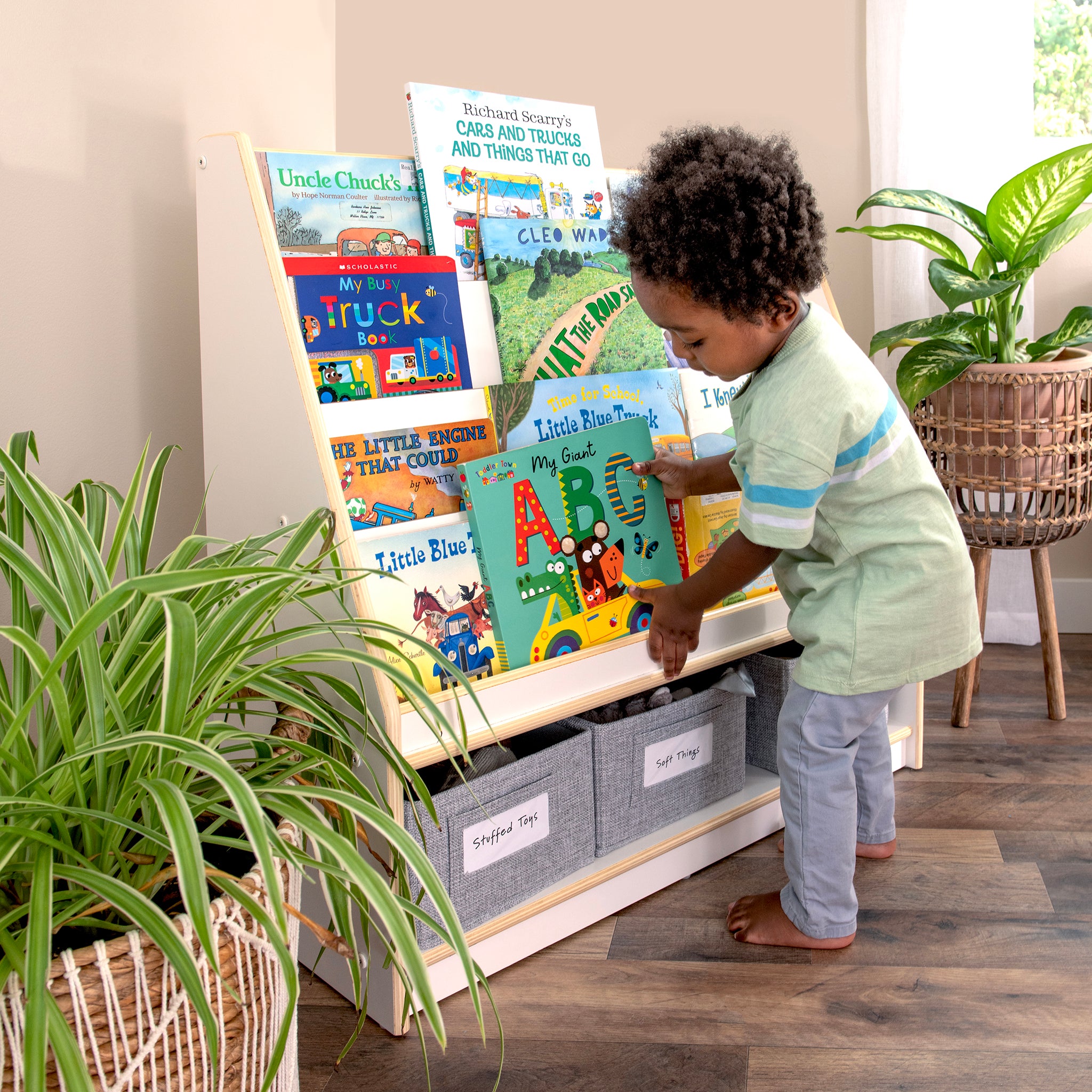 A young child selects a story from a colorful bookshelf in a cozy, plant-filled sanctuary.