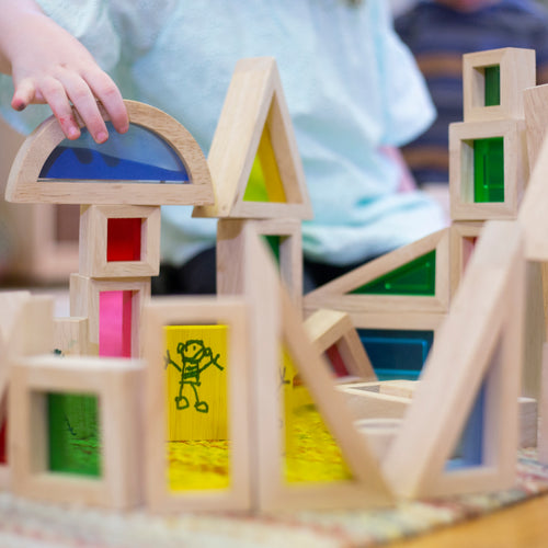 A child creates a vibrant wooden block structure featuring stained glass shapes on a table.