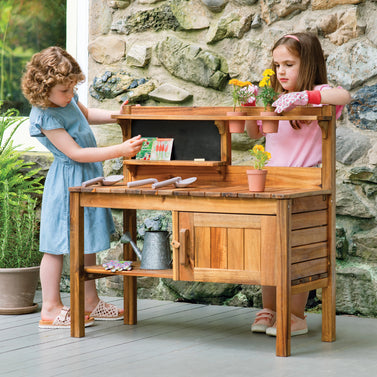 Two children playing with a wooden play kitchen set outdoors.
