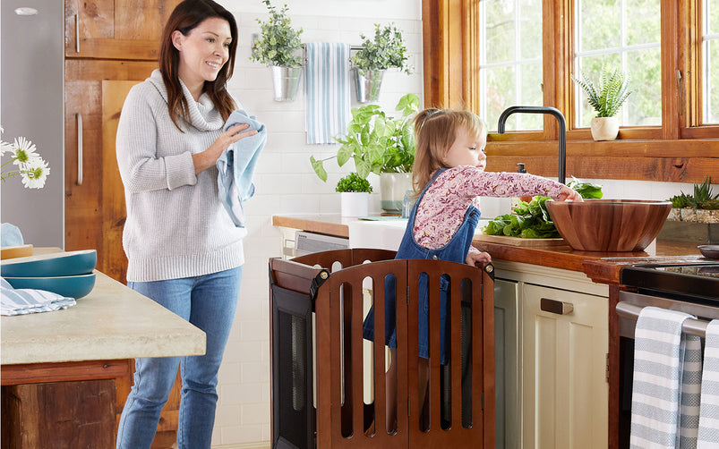 A woman dries dishes as a young girl helps wash fresh vegetables at the kitchen sink.