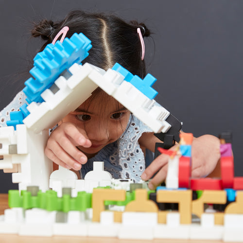 A young girl intently builds a colorful structure with building blocks on a table, her focus sparking creativity.
