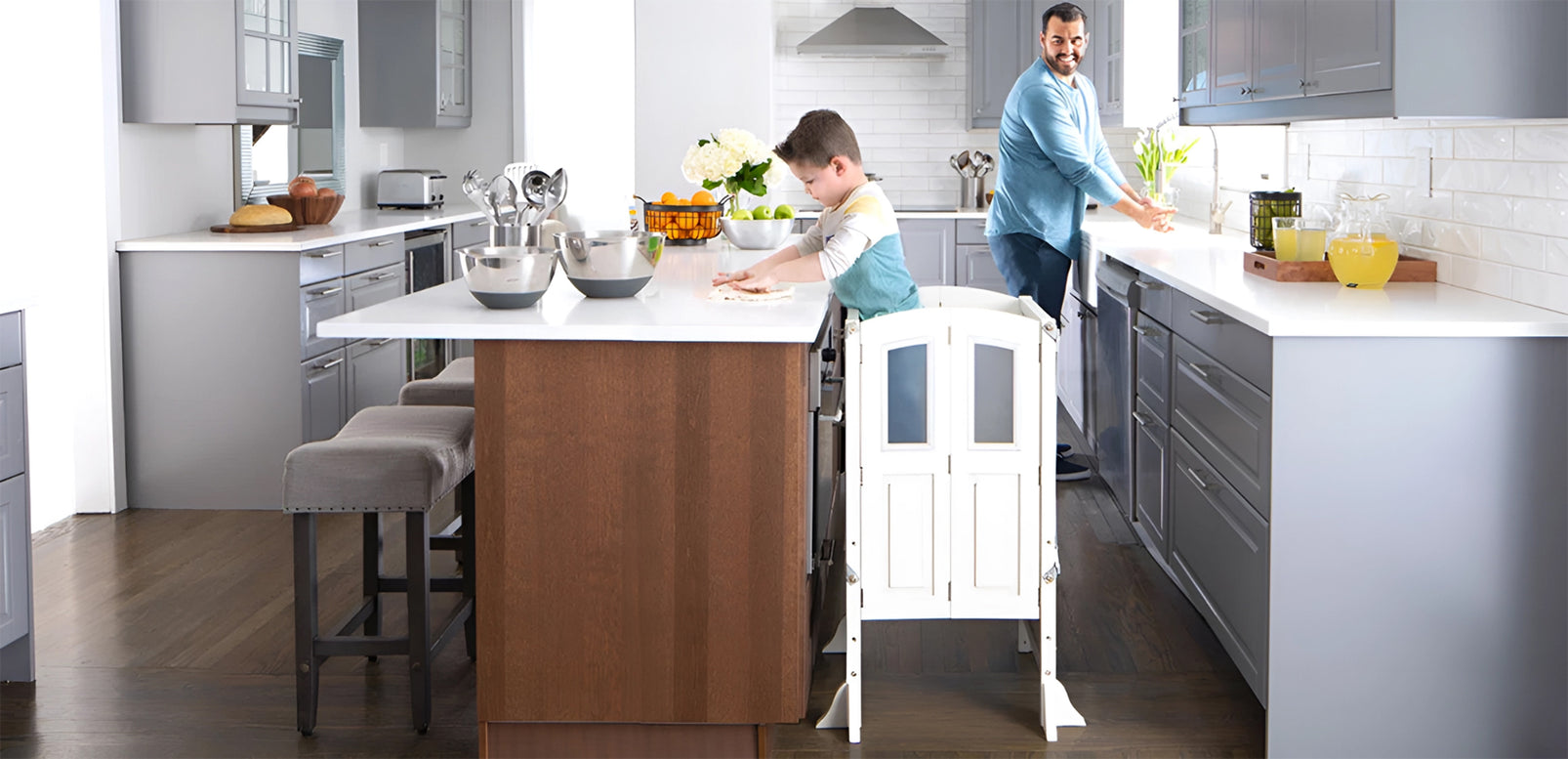 A child and a parent prepare food together in a modern kitchen with gray cabinets and white countertops, enjoying quality time in a stylish setting.