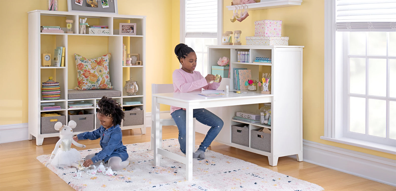 Two children play and craft in a bright, organized room filled with shelves, toys, and a wooden desk.