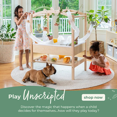 Two young girls and a French bulldog enjoy a wooden activity table with tubes in a bright, cheerful living room.