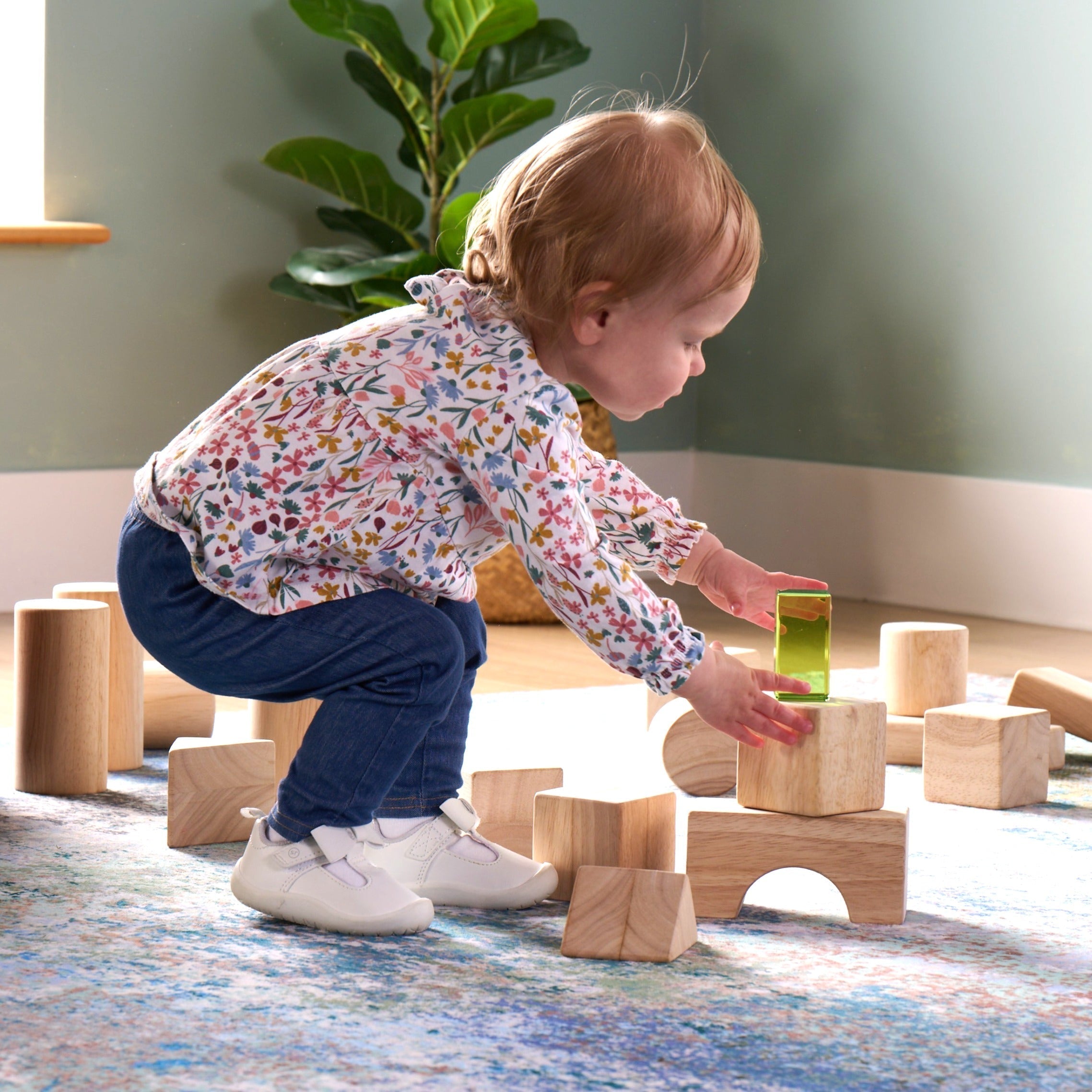 Toddler girl stacking an acrylic block on top of wooden blocks
