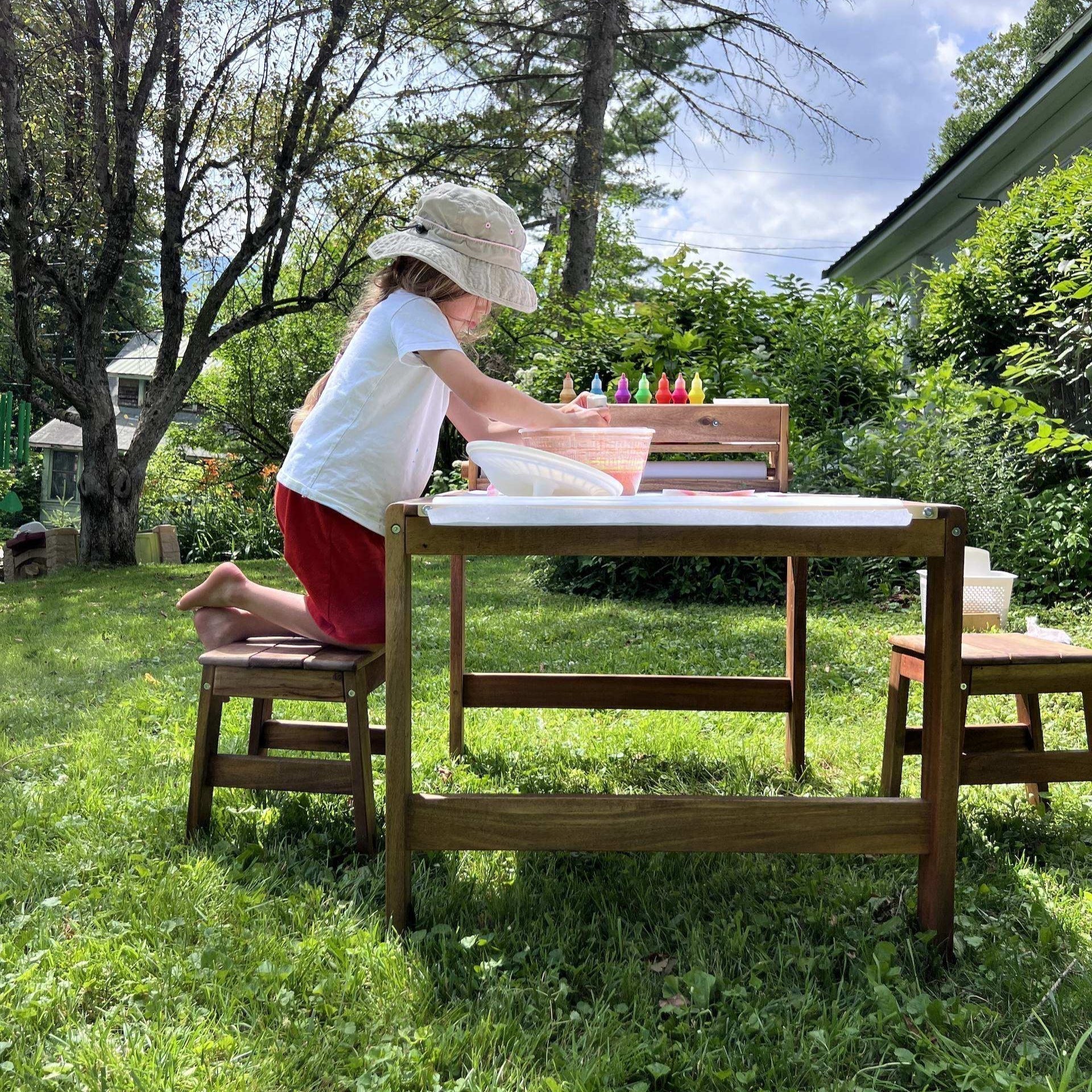 A young boy using paint to create art outside on the Acadia Outdoor Art and Activity Table
