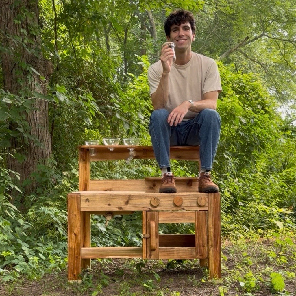 Guidecraft Designer, David Ingle, sitting with the Acadia Outdoor Mud Kitchen that he designed