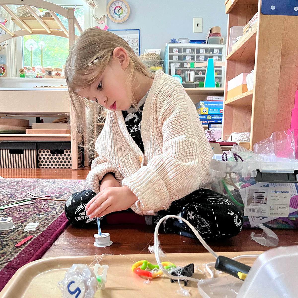 Young child sitting on the floor of their playroom, constructing and building with various loose parts, small found and manufactured objects