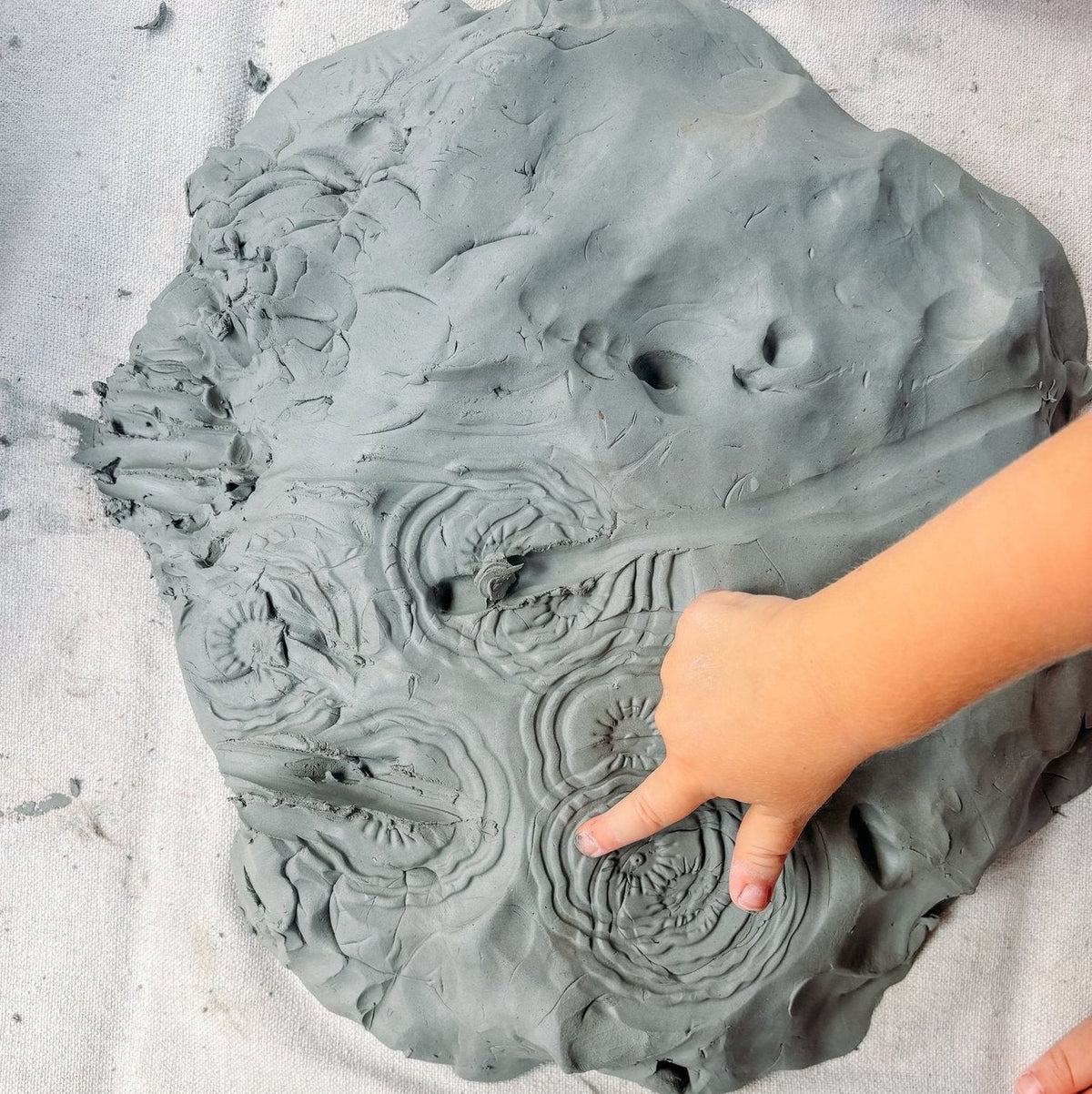Children's hand playing with a large piece of clay