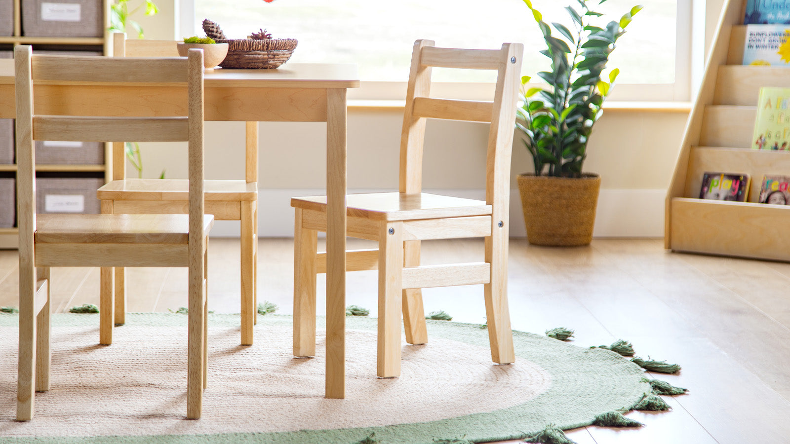 Light wood table and chairs on a round rug in a bright, cozy room with plants and bookshelves.