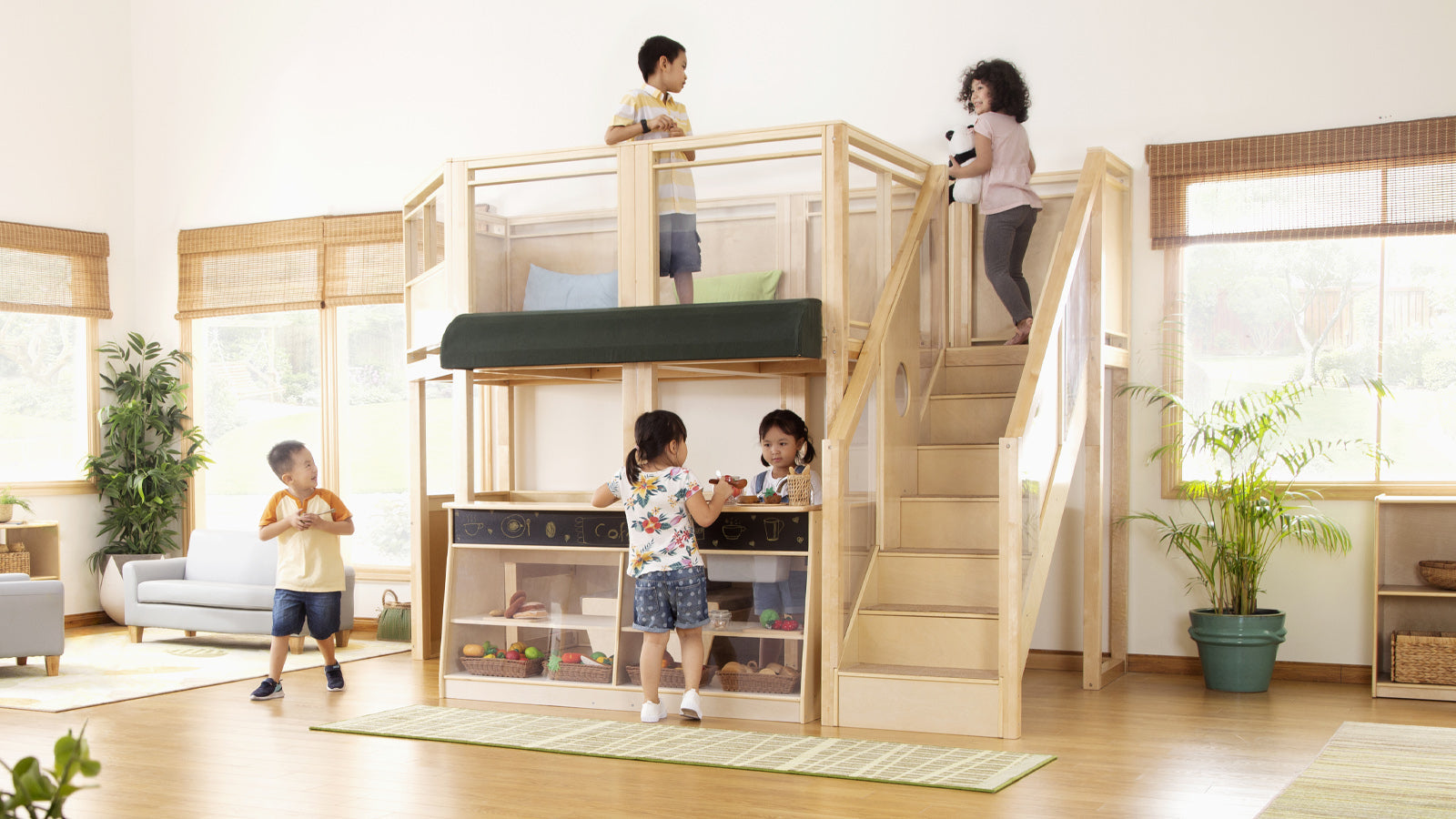 Five children play on and around a wooden indoor play structure with stairs and a play kitchen in a bright room.