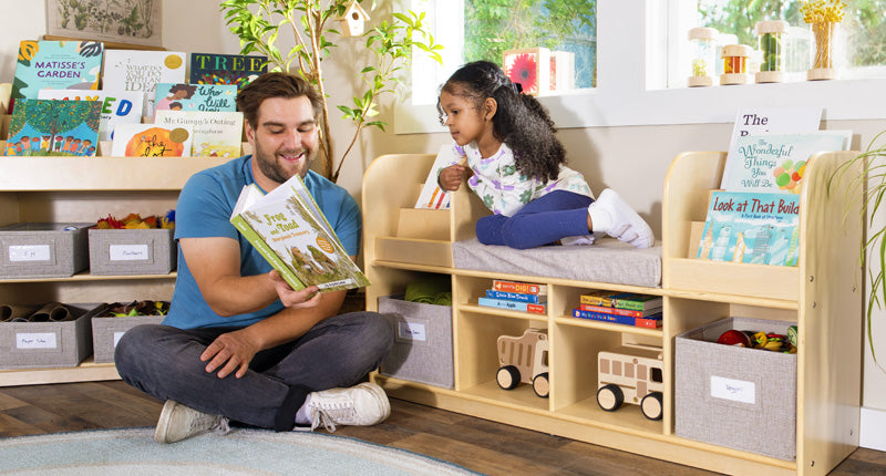 Classroom scene featuring natural birch wood furniture with several children and a teacher making artwork at a table surrounded by plants and art