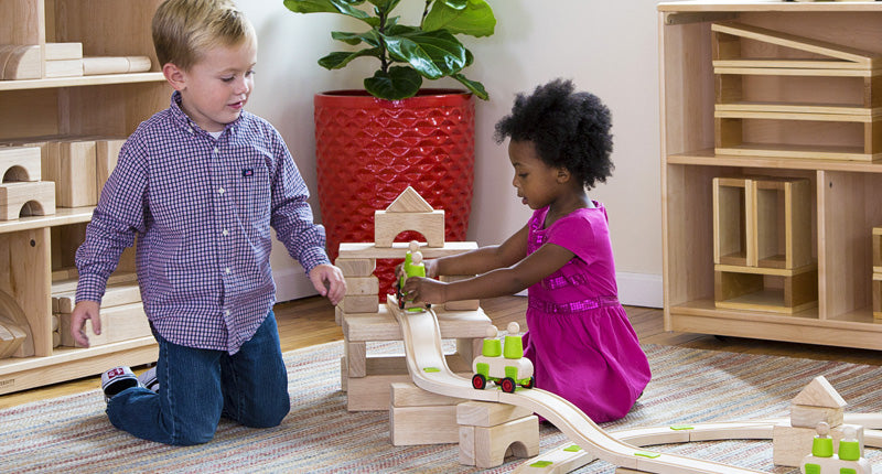 Two children building with a wooden toy track and car set and unit blocks