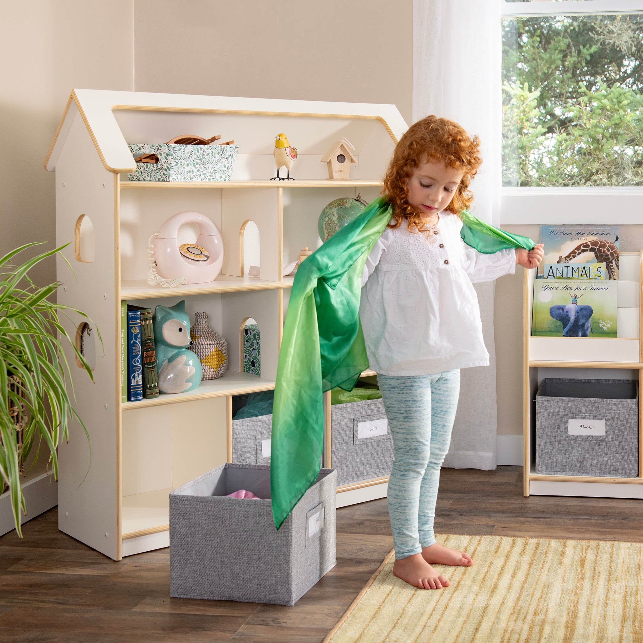 Young girl in front of open shelving montessori dollhouse with bins