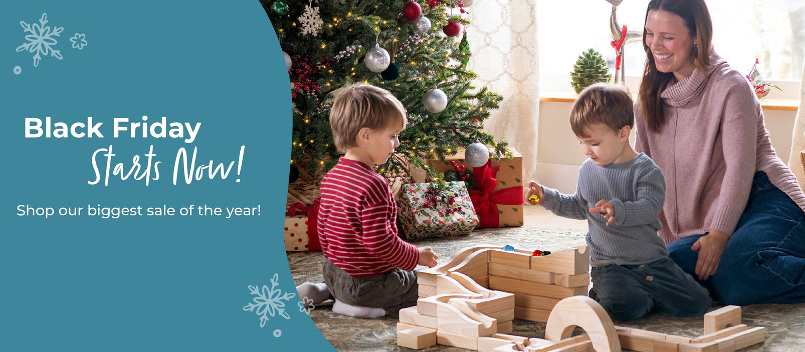 Woman and children playing with a toy block set in a festive room with a Christmas tree, promotional text stating Black Friday Starts Now! Shop our biggest sale of the year!.