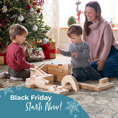 Woman and children playing with a toy block set in a festive room with a Christmas tree, promotional text stating Black Friday Starts Now! Shop our biggest sale of the year!.
