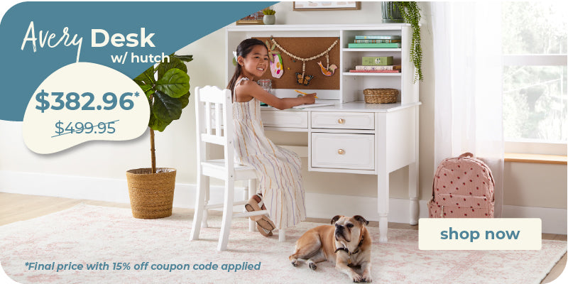 A white children's desk with a hutch and attached chair in a bright room, shown with a girl sitting at the desk, a dog on the rug, and a pink backpack nearby. Promotional text reads 'Every Desk w/ hutch' and includes a 'shop now' button.