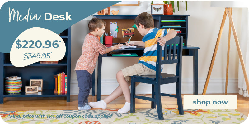 A children's media desk setup in a bright room, featuring a dark navy blue desk and hutch with a matching chair. Two young boys are shown sitting at the desk, writing and interacting.