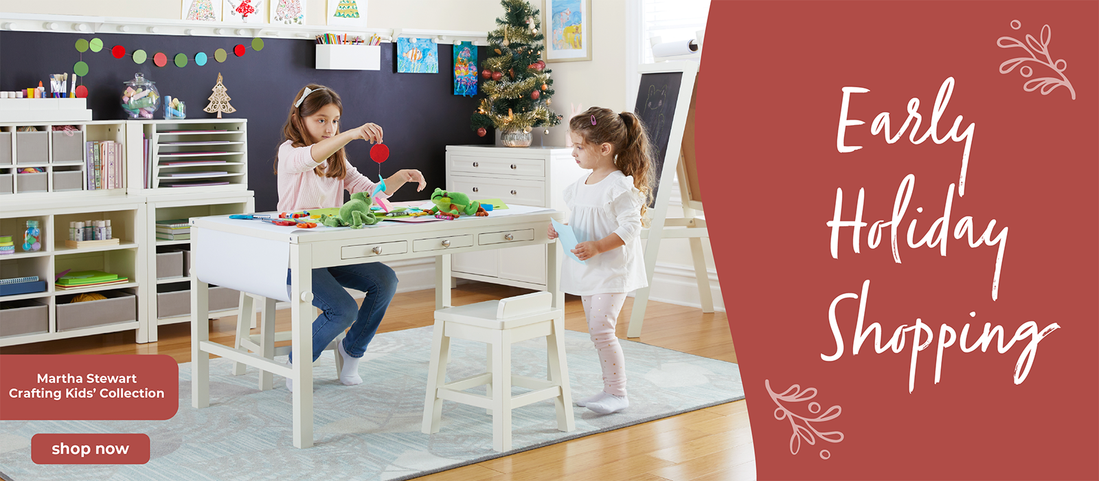 Two children playing at a Martha Stewart art table with craft supplies in a children's art room setting, featuring 'Early Holiday Shopping' text on a red banner.