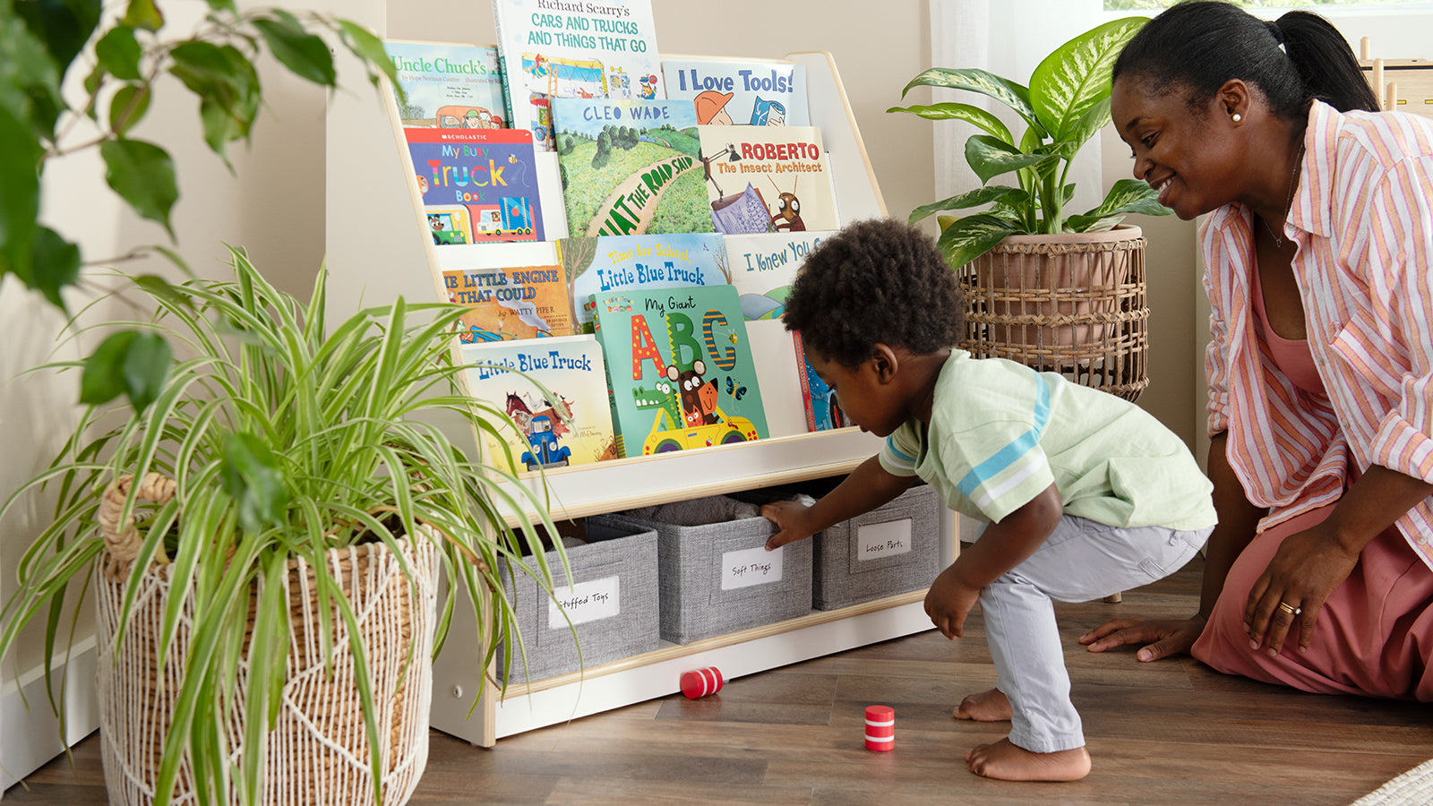 Mother and young child sitting on floor, child choosing a toy from the cloth bin