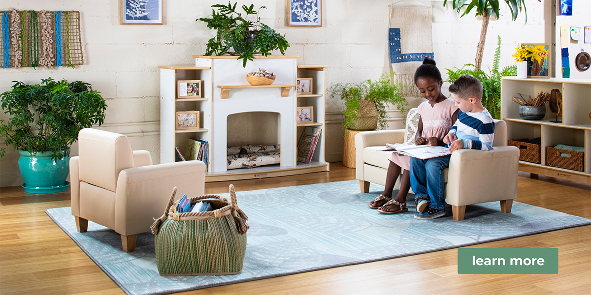 2 children sitting on a small couch reading a book together in a bright, clean, nature-filled classroom with calming blue, green and neutral touches. This is a banner for environmental classroom design services through Guidecraft.