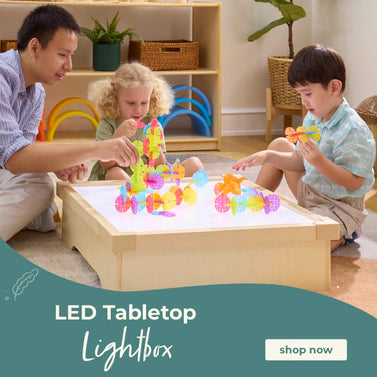 Children playing with colorful toys on a LED tabletop lightbox in a home setting.