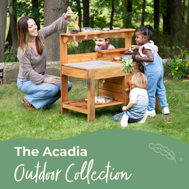 Woman and children playing with a wooden play kitchen set outdoors, with 'The Acadia Outdoor Collection' text.