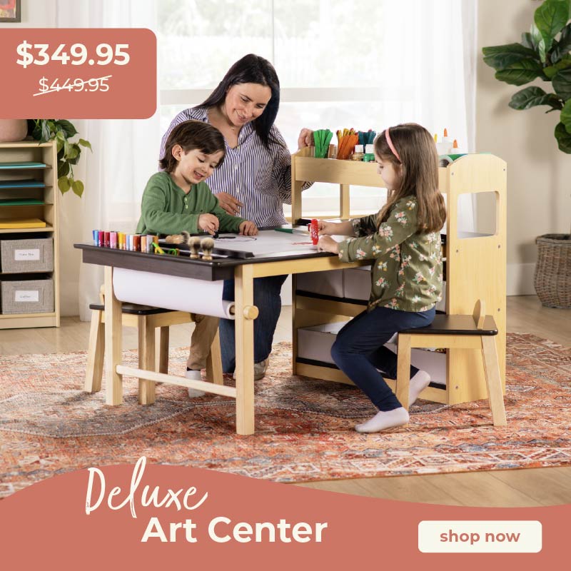 Two children and a woman at a wooden art center with supplies, promotional text overlay. Click to shop the Deluxe Art Center on sale for $349.95 down from $449.95