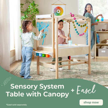 Children playing with a Sensory System Table with Canopy and Easel in a bright room. Click to shop the easel and table on sale now.