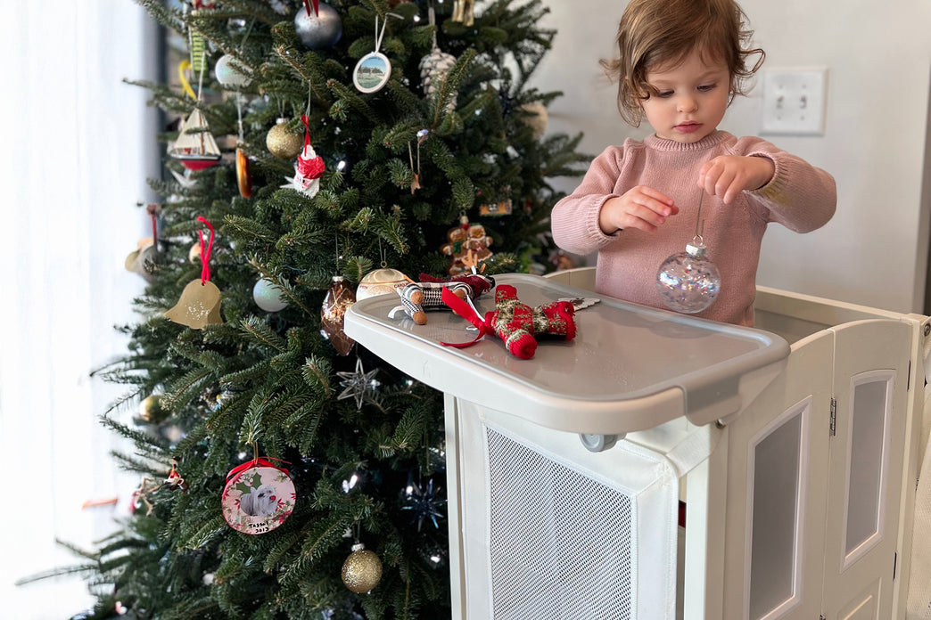 Child decorating a Christmas tree with ornaments in a home setting. Click to shop all Kitchen Helpers and toddler towers
