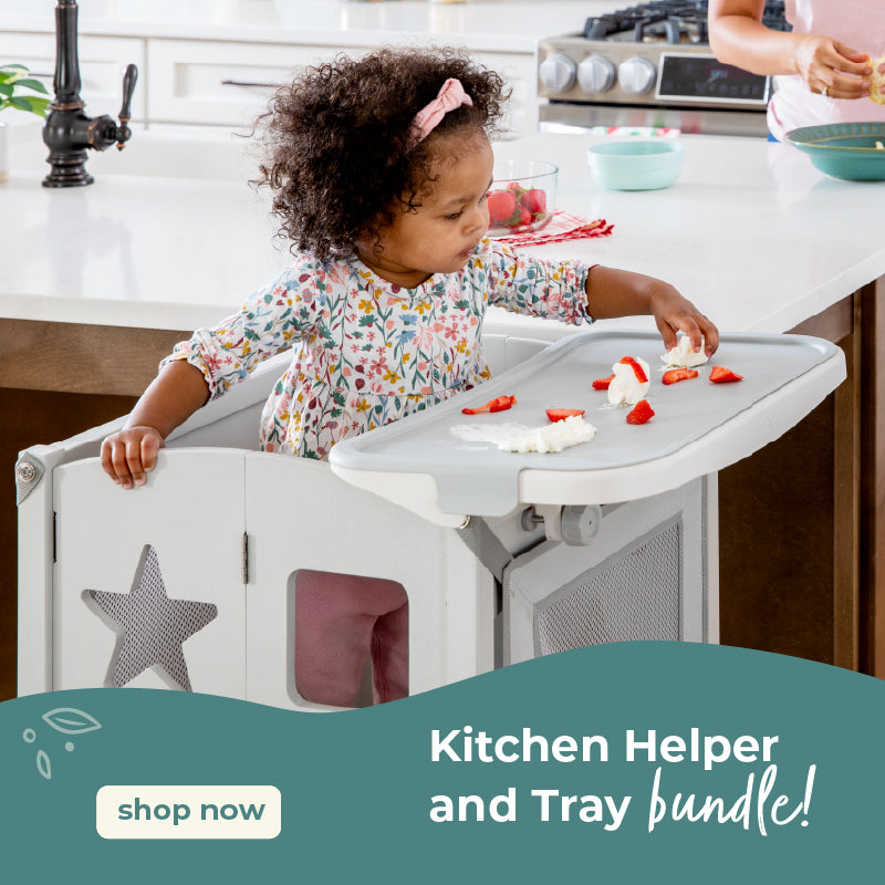 Child in a kitchen helper and tray bundle in a kitchen. Click to shop kitchen helper bundles.