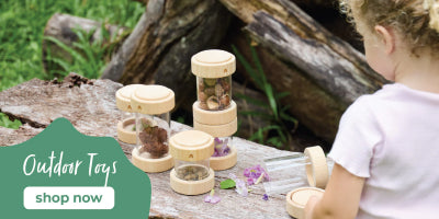 Child playing with wooden outdoor toys on a wooden surface with a natural background.
