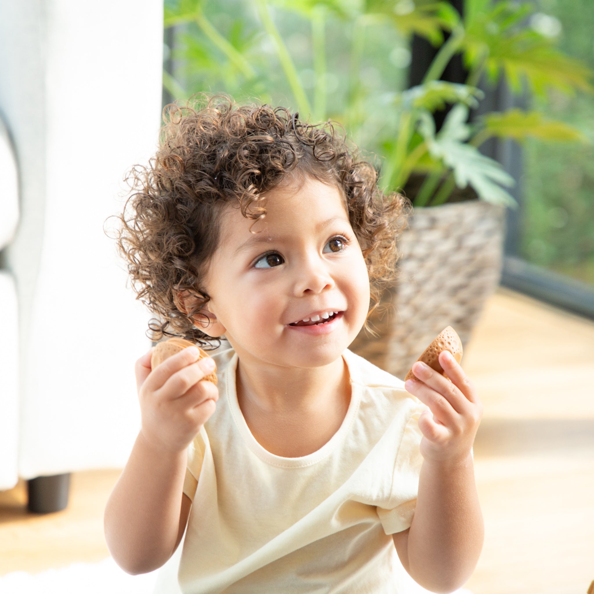 Child holding two pieces of bread indoors with a plant in the background