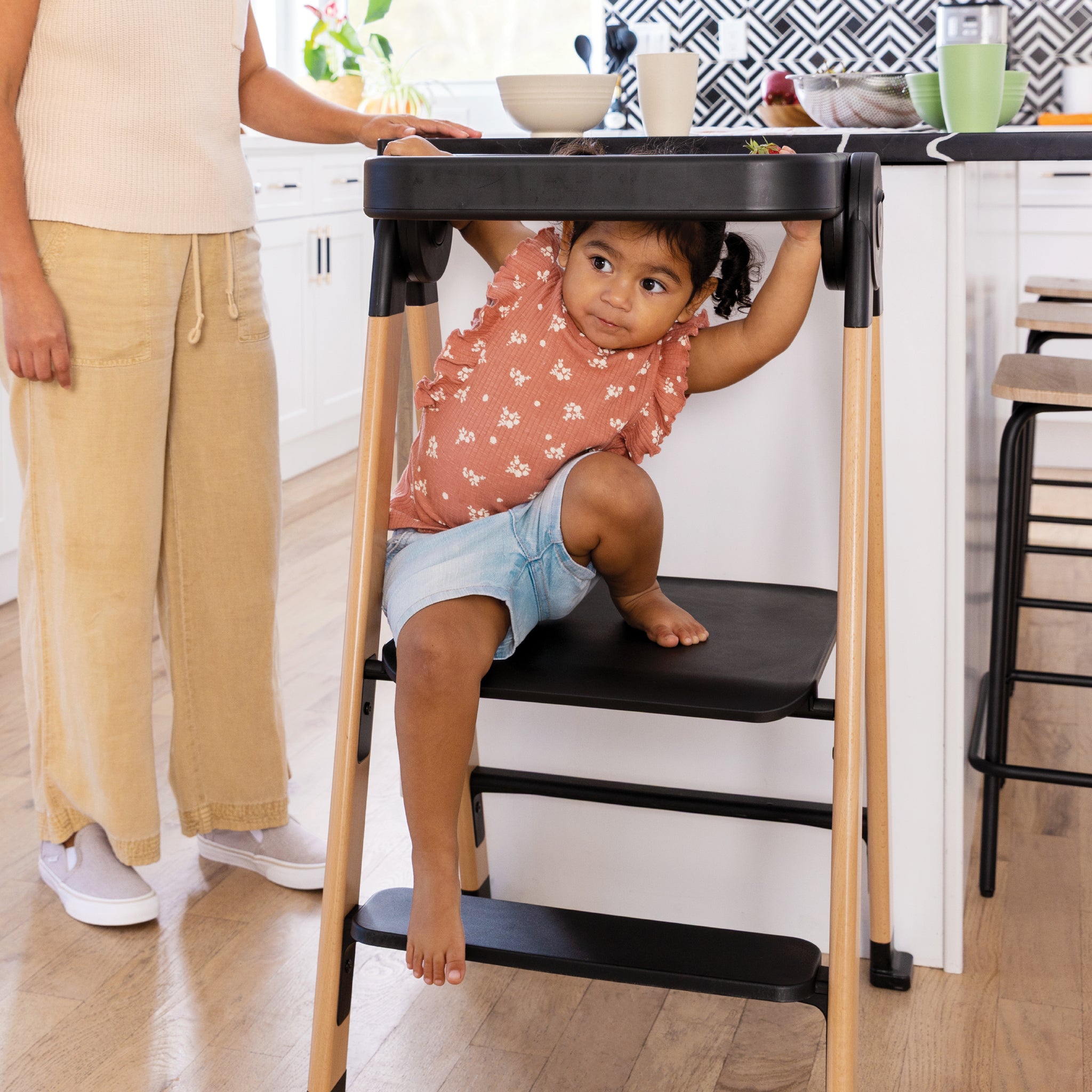 Child on a high chair in a kitchen with an adult nearby