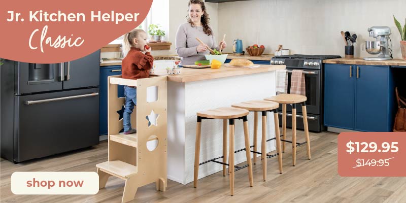 Mother and child at a kitchen island, child in a junior kitchen helper. Click to shop the Jr. Kitchen Helper Classic for $129.95