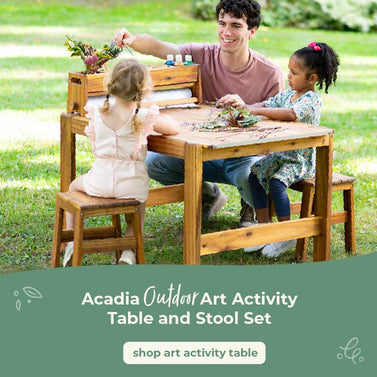 Two children and a adult sitting at an outdoor art activity table in a grassy area. Creating art on the Acadia Art Activity Table. Click to shop the art table.