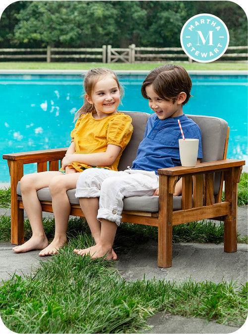 Two children sitting on a wooden bench by a pool 