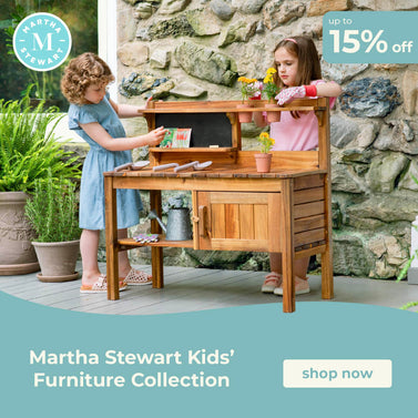 Two children playing with a wooden play kitchen set outdoors, with a promotional banner for Martha Stewart Kids' Furniture Collection.