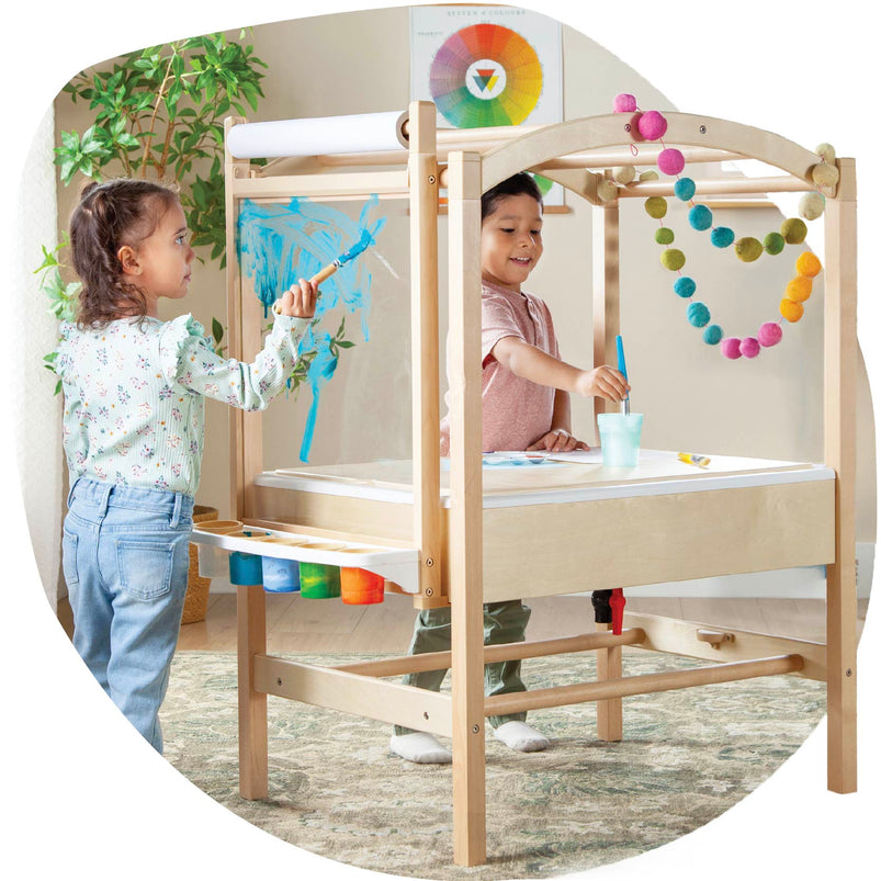 Two children playing with a wooden playhouse.