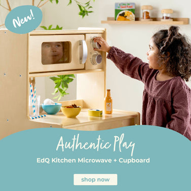 Child playing with a wooden kitchen set, including a microwave and cabinet, with text about 'Authentic Play' on a light blue background. Click to shop all play kitchens