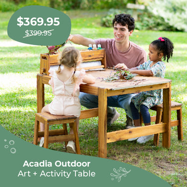Family with children at a wooden outdoor art activity table in a park, click to shop $30 off the Acadia Outdoor Art and Activity Table.