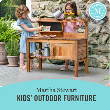 Two girls watering plants on the Martha Stewart Outdoor Potting Bench, click to shop all Martha Stewart Kids' Outdoor Furniture.
