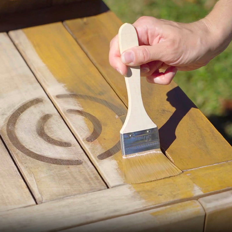 Person applying wood stain to a wooden surface with a brush